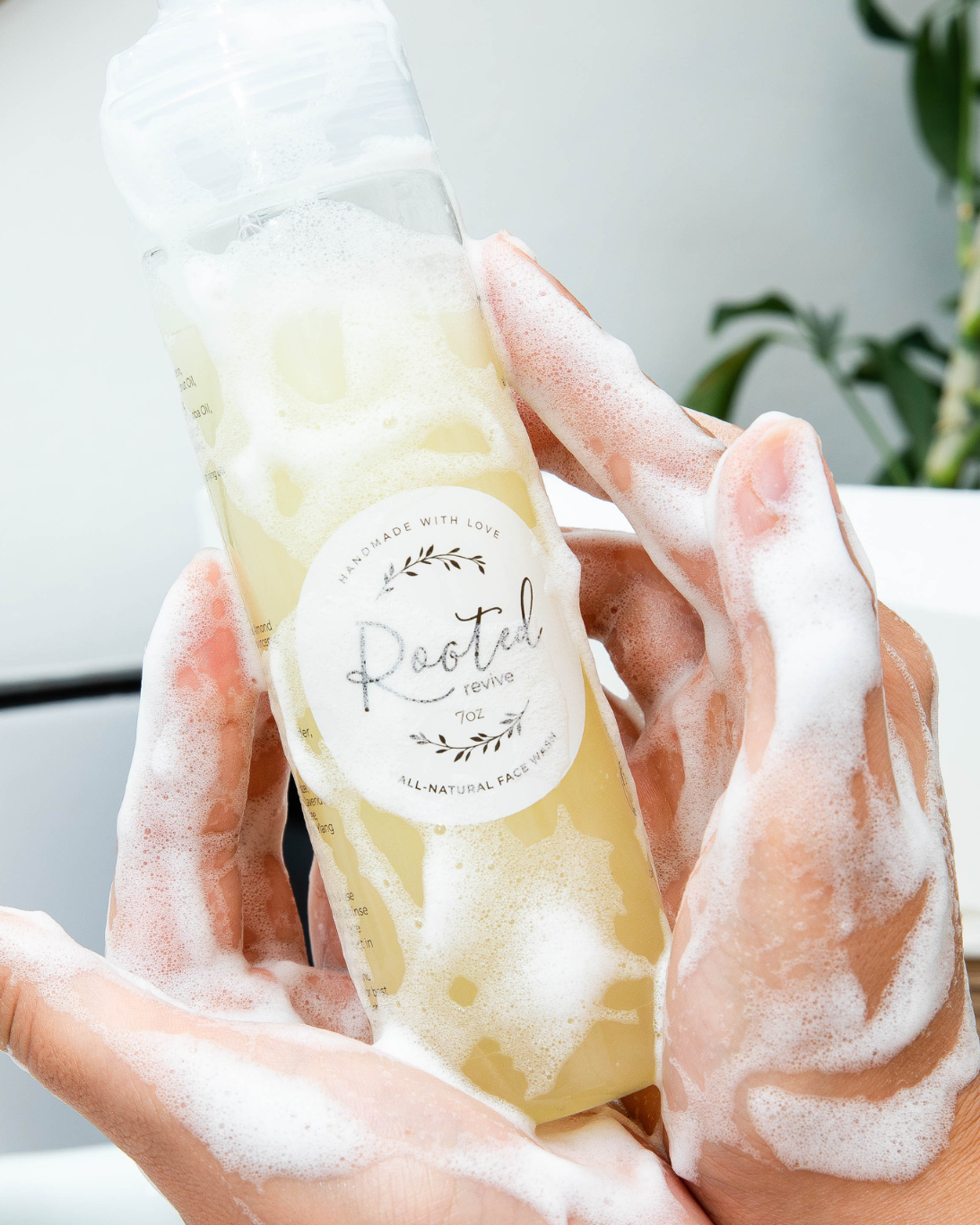 Person holding a bottle of soap with a soapy hand, in a bathroom setting.