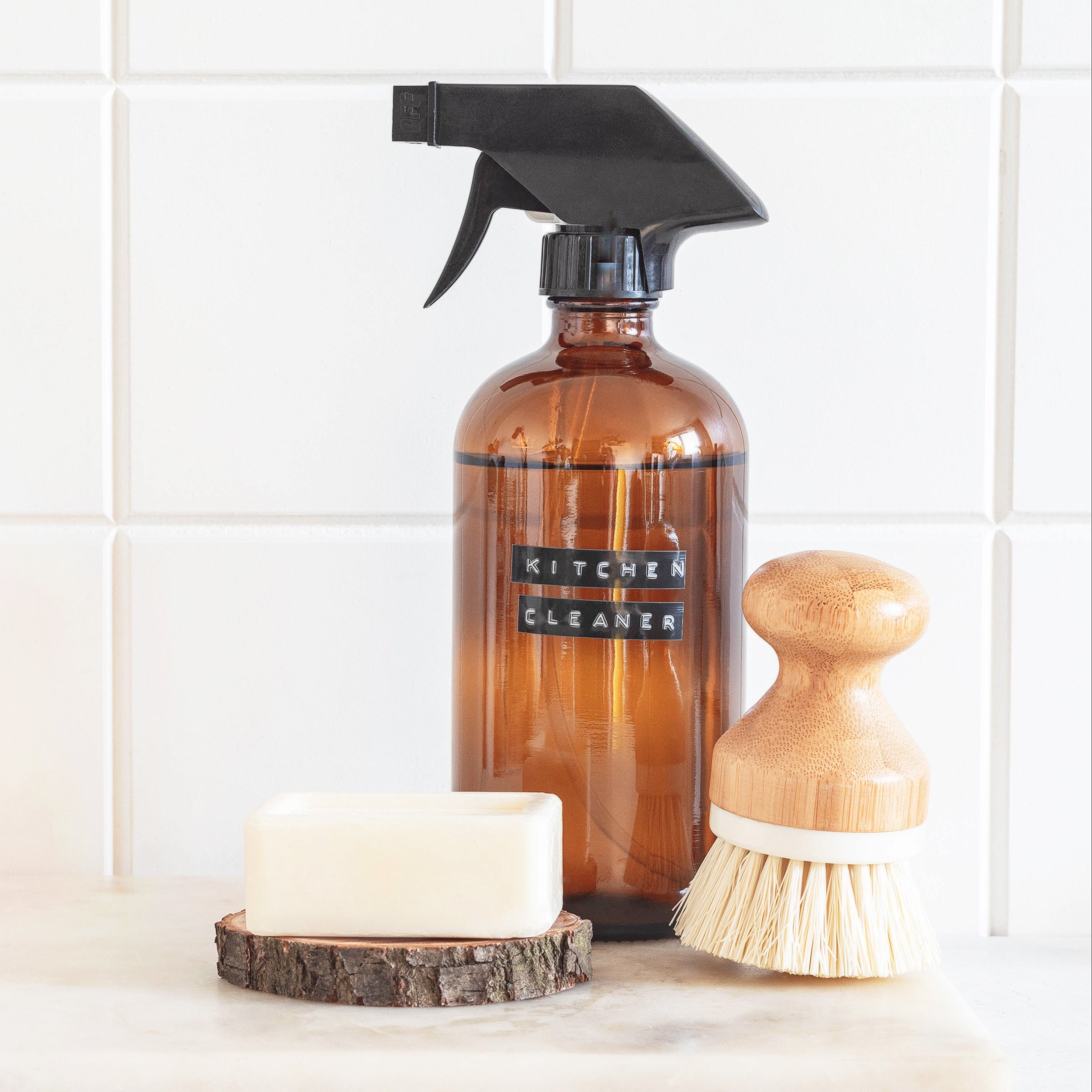 Brown spray bottle labeled 'Kitchen Cleaner' on a white surface with a tiled wall background